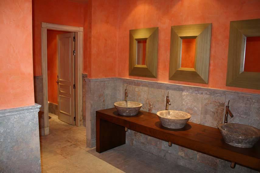 Mueble encimera en madera , paredes con pintura al estuco.Parte inferior con zocalon de marmol travertino rojo con poro abierto.
